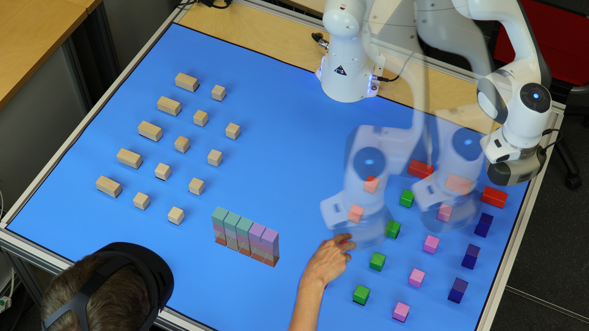 Human and industrial robot work cooperatively on a building block task. Virtual objects indicate the final state and the robot motion.